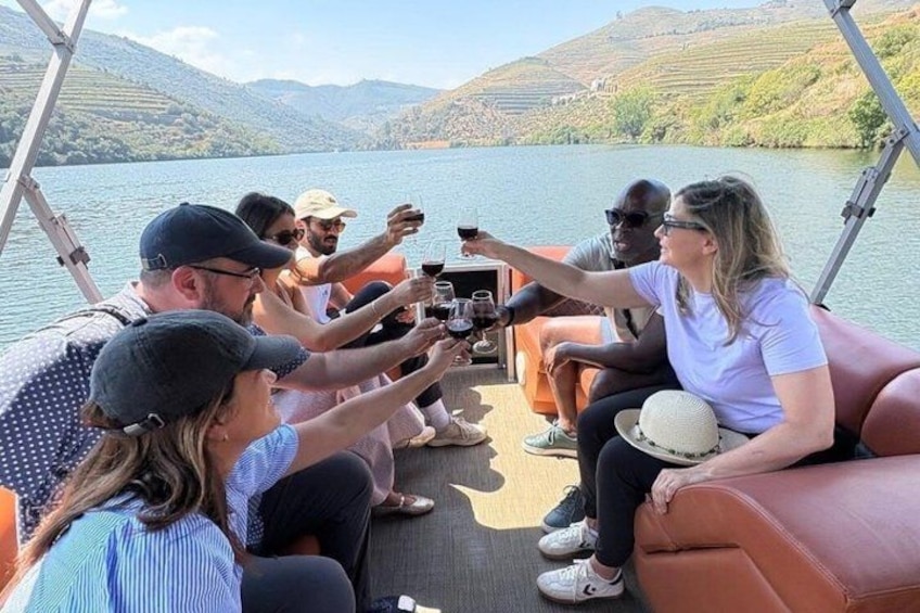 Un groupe de personnes se trouve sur un bateau, certaines tenant des verres à vin, avec un lac et des collines en arrière-plan. 2