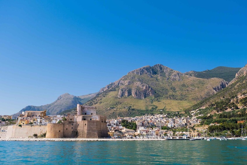 Een kustplaats met een historisch fort, een haven vol boten en bergen op de achtergrond. 4