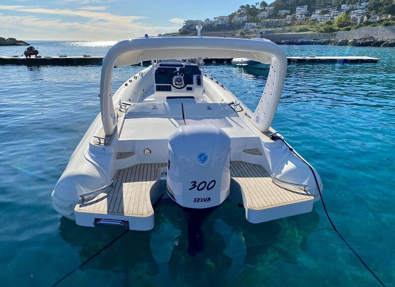 Een witte motorboot met een cabine en een motor van 300 pk, afgemeerd aan een steiger met helderblauw water en huizen op de achtergrond. 3