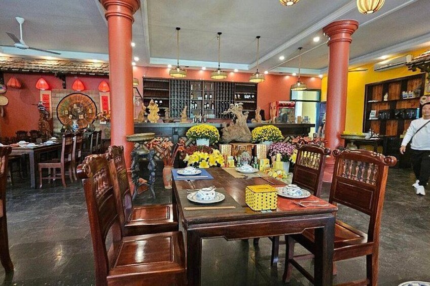 Interno di un ristorante con tavoli e sedie in legno, pilastri rossi e fiori decorativi. 3