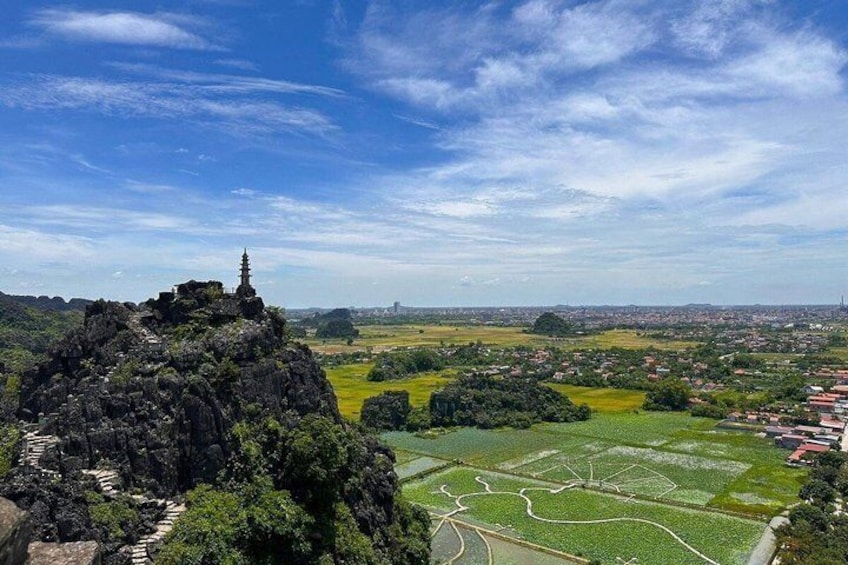 Un paisaje montañoso con un templo en la cima, campos en terrazas abajo y un horizonte urbano distante. 4