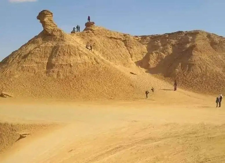 A desert landscape with a prominent rock formation and several people exploring the area. 3