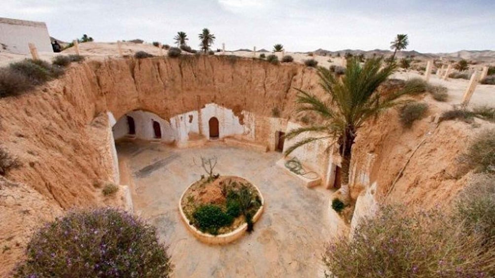 A traditional terraced structure with arched doorways, surrounded by desert vegetation and palm trees. 2