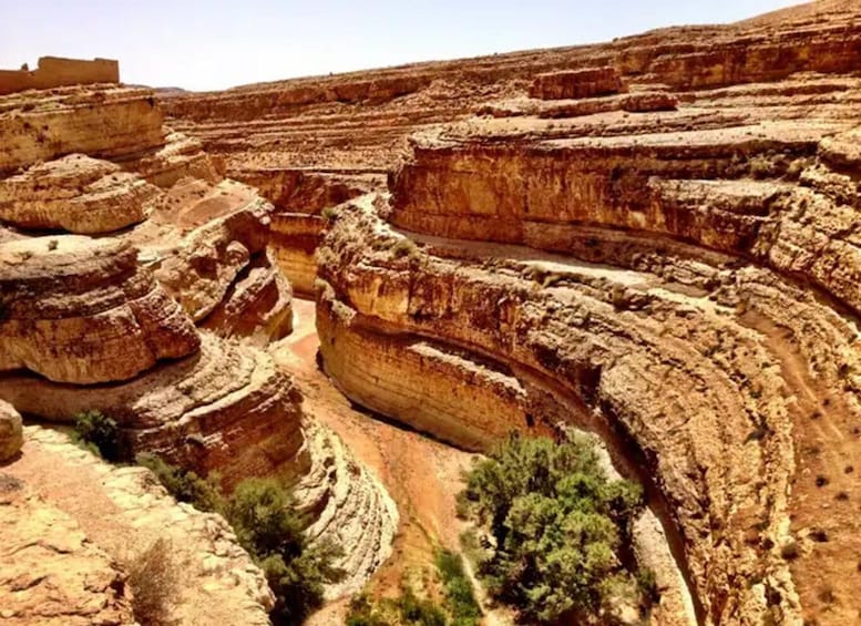 A rugged canyon landscape with layered rock formations and sparse vegetation. 5