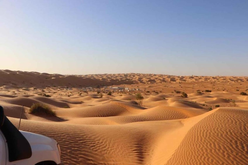 A desert landscape with sand dunes and a small settlement in the distance. 1