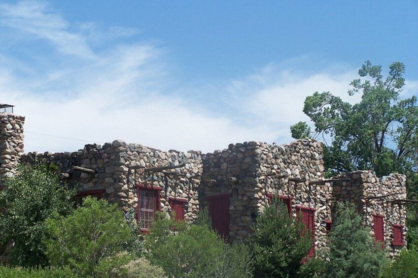 A stone building with red doors and windows, surrounded by greenery. 3