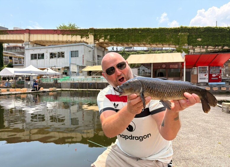 A person holding a fish near a body of water with buildings in the background. 1