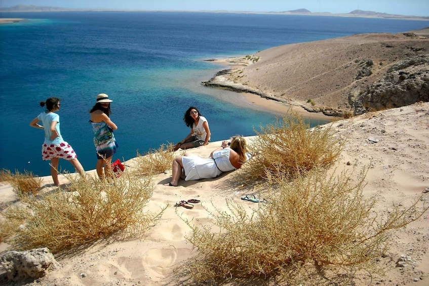 A group of people on a sandy beach with a view of the sea and distant hills. 2