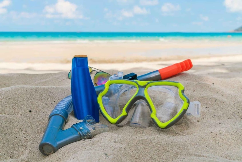 Snorkeling gear, including a mask and snorkel, on a sandy beach with a clear blue ocean in the background. 5