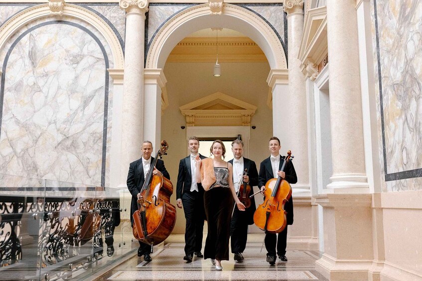A group of musicians in formal attire walking through a grand hall with marble walls and classical architecture. 2