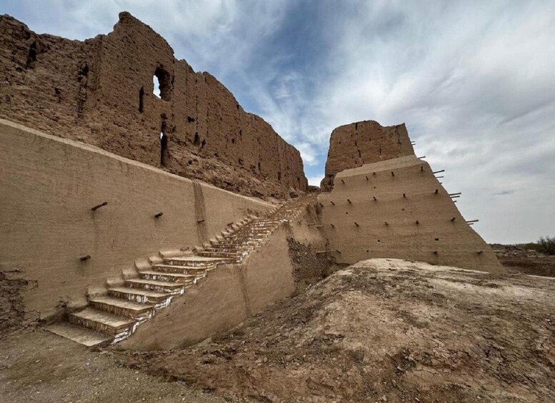 A desert landscape with ancient ruins, including a large stepped structure and a pyramid-like formation. 1