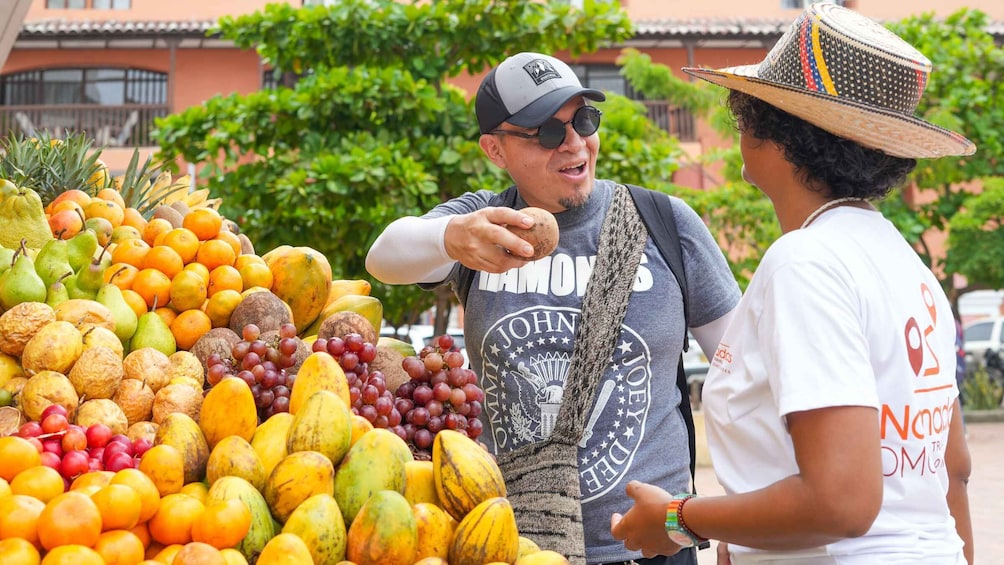 A fruit stand with various fruits and a person pointing at the display. 1