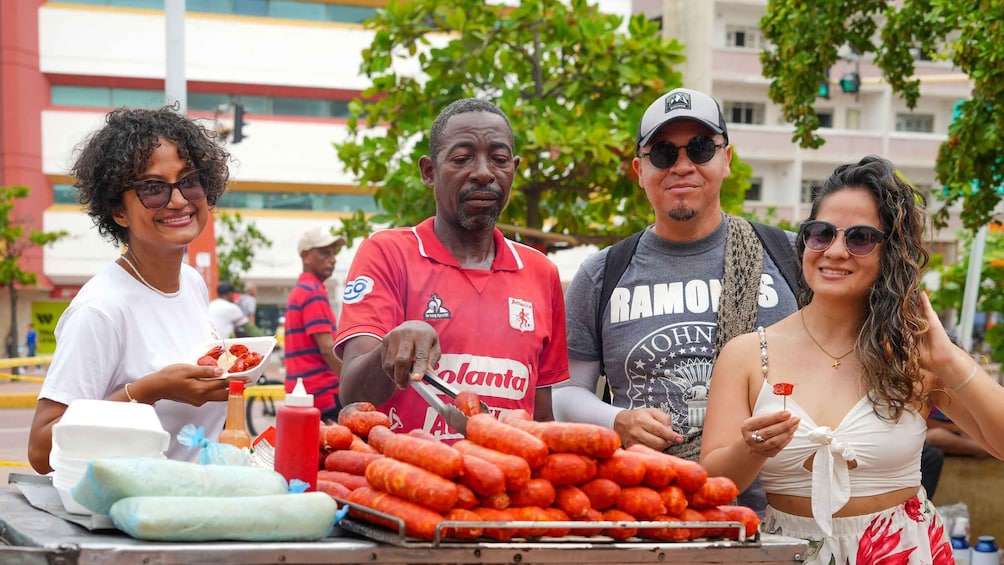 A street food vendor with a cart of sausages and condiments, people eating, and a building in the background. 3