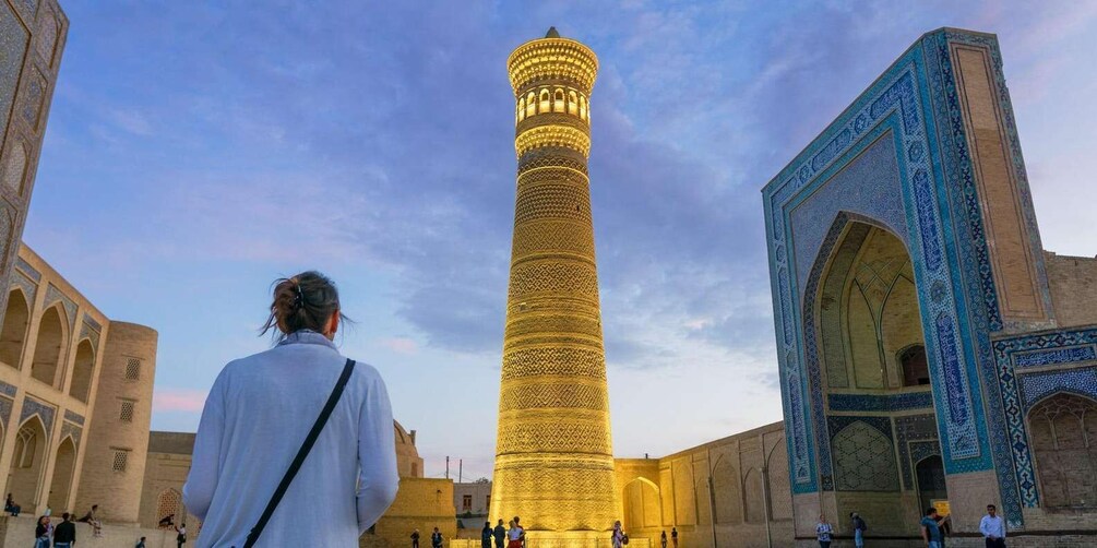A tall, intricately patterned minaret in a courtyard with a large, ornate archway. 1