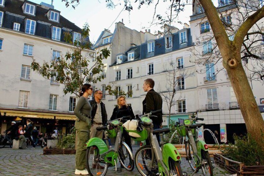 A group of people standing around bicycles in an urban setting with buildings in the background. 3