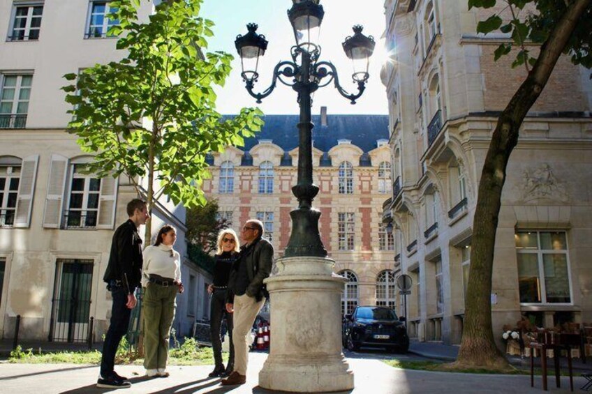 A group of people standing by a street lamp in an urban setting with historic buildings in the background. 1