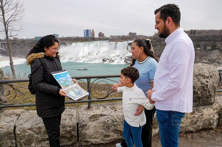 A family standing by a waterfall with a rocky foreground and a cityscape in the background. 2