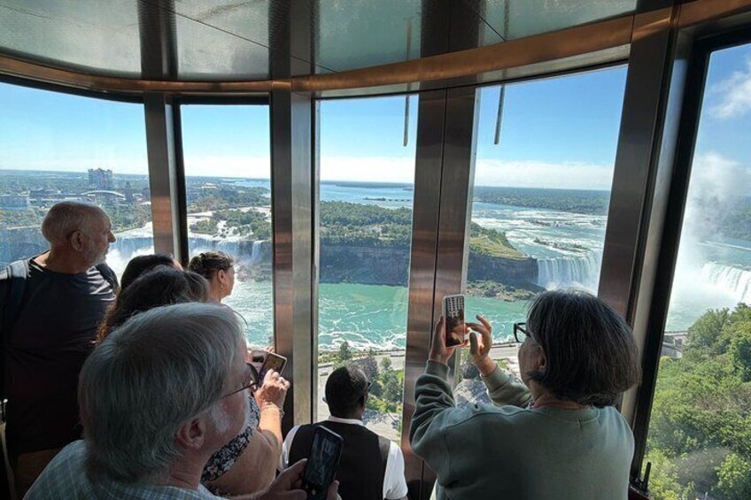 A group of people inside a glass observation area, looking out at a waterfall and surrounding landscape. 1