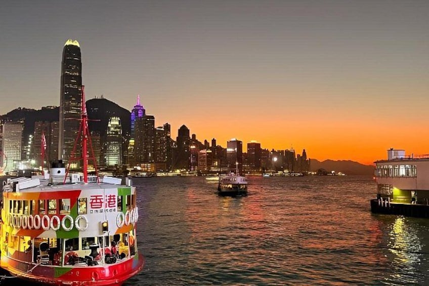 A city skyline at sunset with illuminated buildings, a river with boats, and a prominent skyscraper. 1
