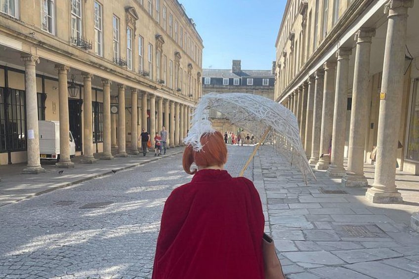 Una persona con una camicia rossa cammina lungo una strada acciottolata fiancheggiata da colonne. 1