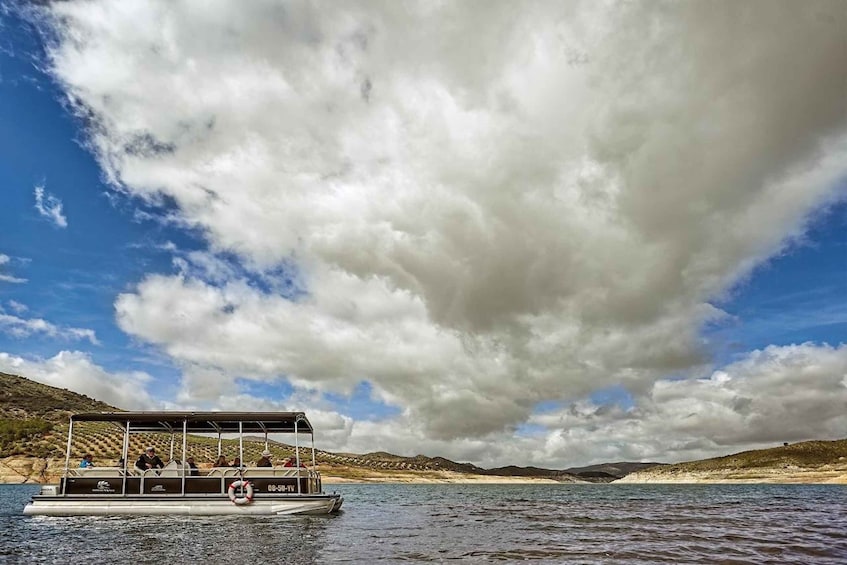 A boat on a lake with passengers, surrounded by a hilly landscape and a cloudy sky. 3