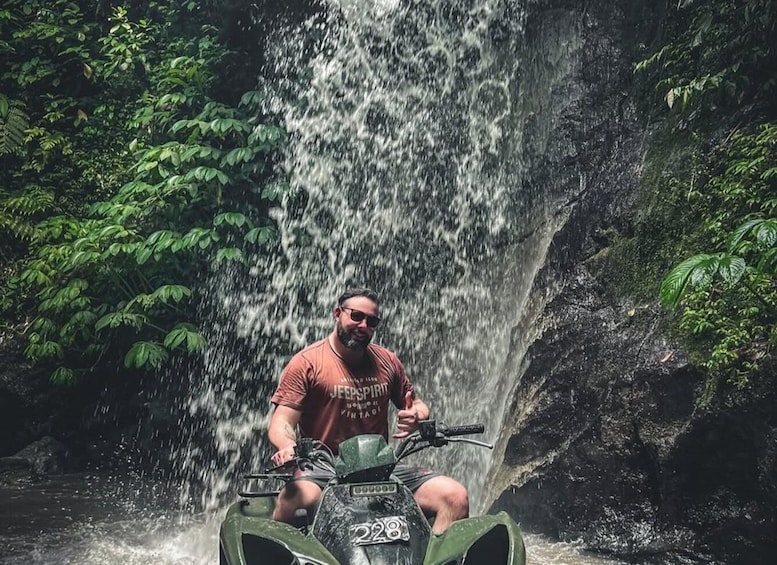 A person on an ATV near a waterfall in a forest. 3