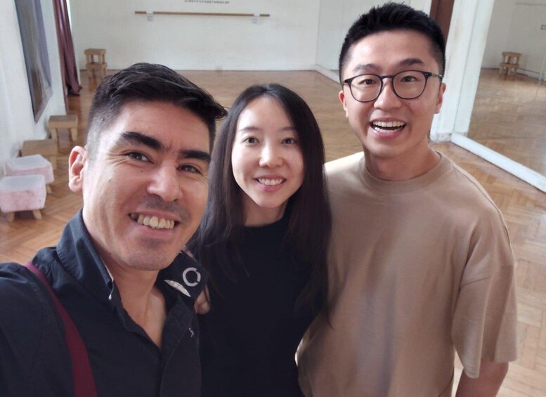 Three people in a room with wooden flooring and a white wall with a hanging object. 2