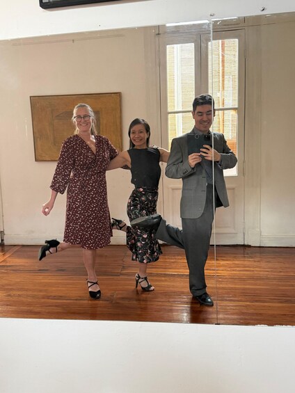 Three people in a room with wooden floors and a painting on the wall. 3
