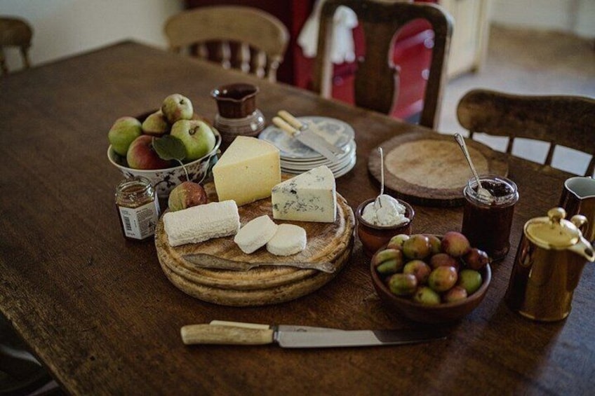 A wooden table with a variety of food items including apples, cheese, and a bowl of olives. 1