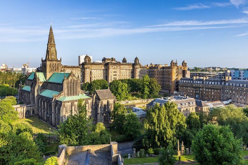 En storslagen katedral med ett högt torn, omgiven av frodig grönska och moderna byggnader. 2