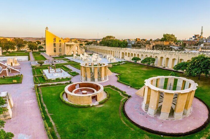 A historical site with circular structures, a large yellow building, and a well-maintained garden. 5