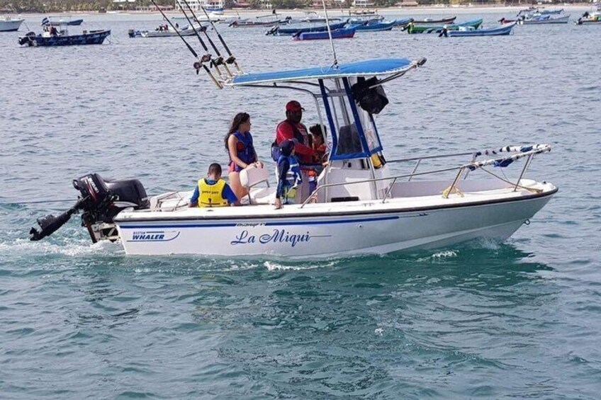 Ein Boot namens 'La Miguei' mit Personen an Bord, umgeben von ruhigem Wasser und anderen Booten in der Ferne. 1
