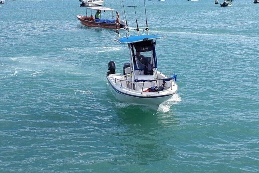 Ein kleines Boot mit blauem Verdeck auf ruhiger See, im Hintergrund weitere Boote. 3