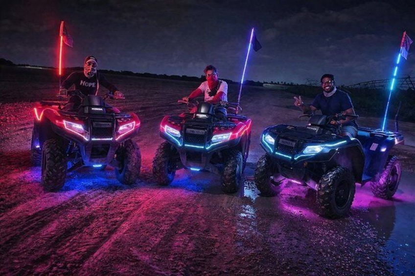 Three ATVs with illuminated lights and flags, parked on a dirt road. 5
