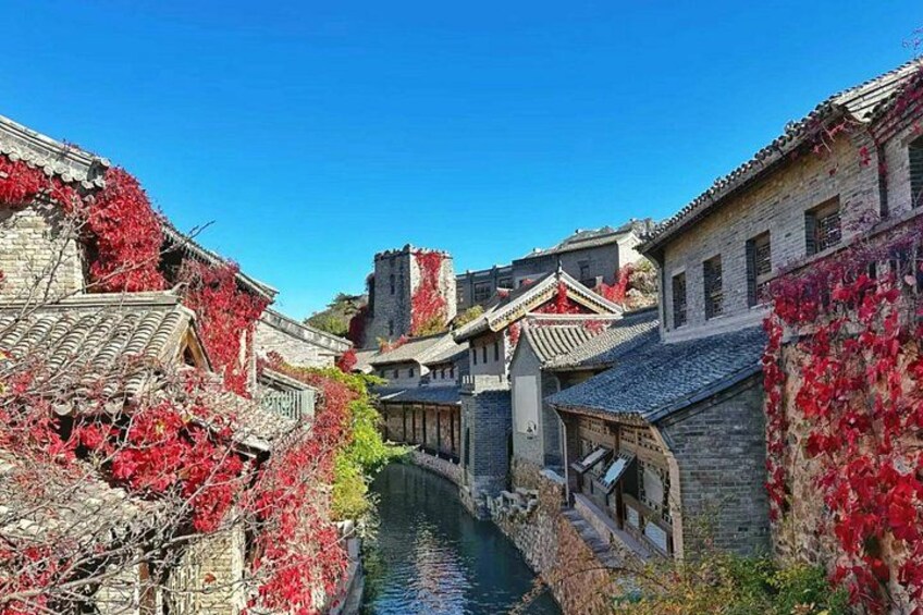 Un canale stretto costeggiato da edifici tradizionali, con autunno che colora il paesaggio, un ponte di pietra e una torre in lontananza. 2
