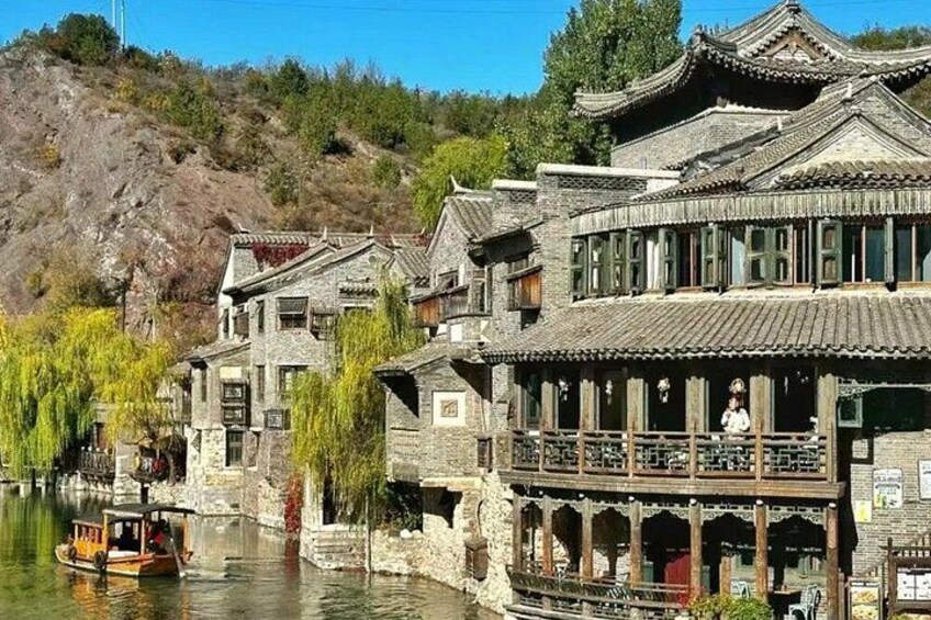Edifici tradizionali lungo un fiume, una barca e una collina sullo sfondo. 1