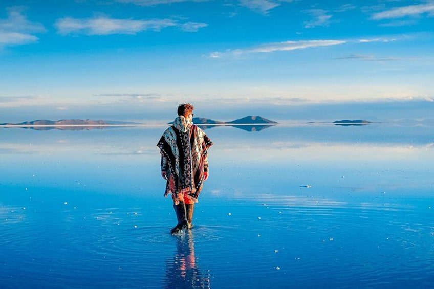 En person står på en reflekterende overflade med en klar himmel og fjerne øer. 4
