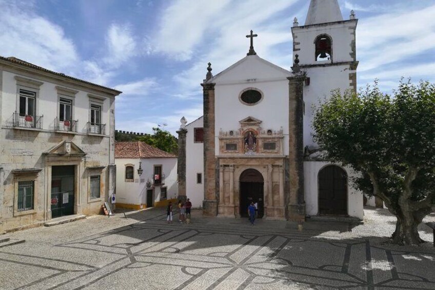 Una iglesia histórica con un campanario, una plaza adoquinada y un árbol. 2
