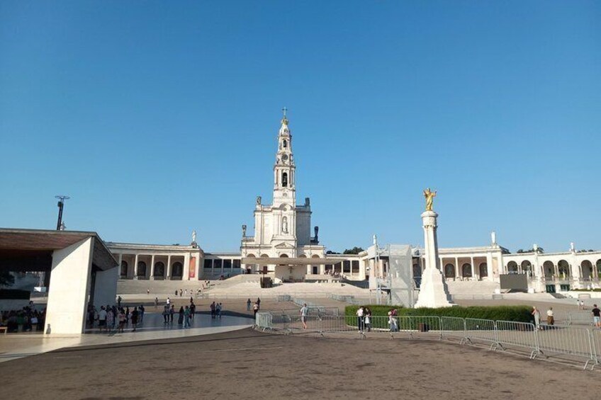 Una amplia plaza abierta con una torre de iglesia destacada, una estatua y un área cercada. 1