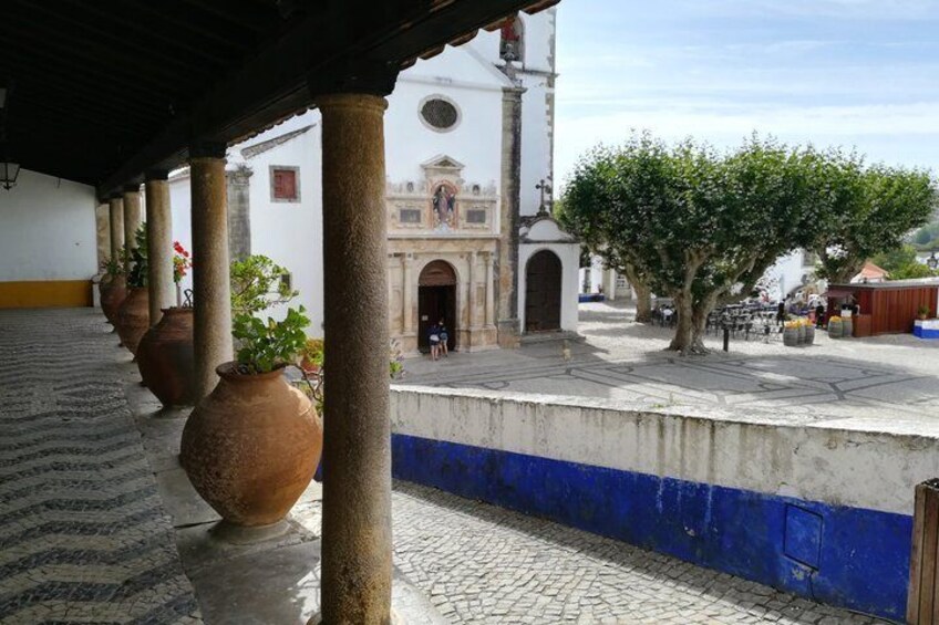 Un patio adoquinado con macetas de barro, un edificio blanco con un campanario y un árbol. 3