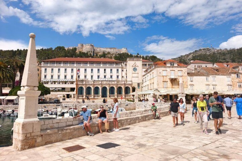A historic waterfront with a prominent building, a stone monument, and a clear view of the sea. 1