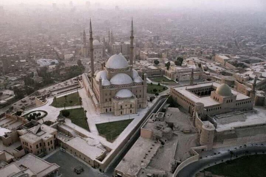Eine große Moschee mit mehreren Kuppeln und Minaretten, umgeben von einer Stadtlandschaft. 1