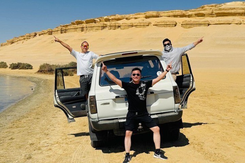 Paisaje des értico con un vehículo blanco y tres personas posando con los brazos levantados. 4