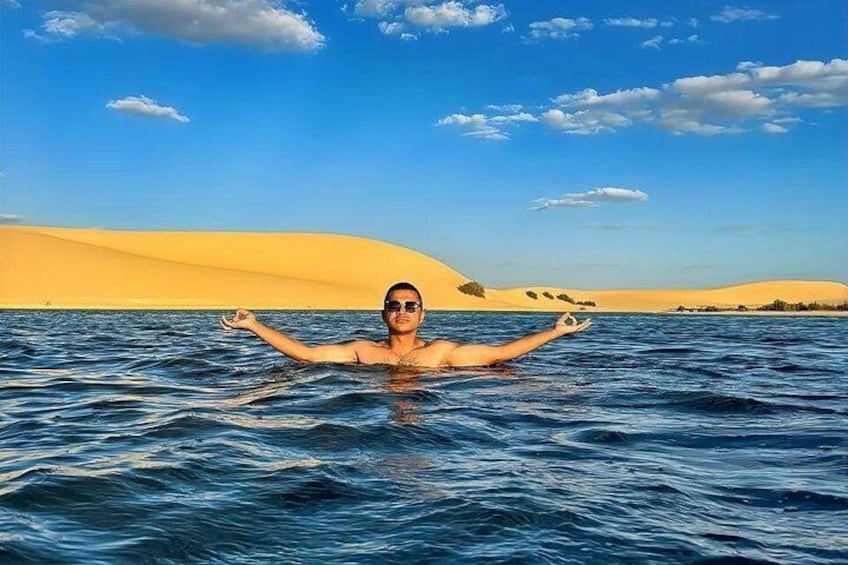 Una persona nada en un cuerpo de agua con dunas de arena al fondo. 3