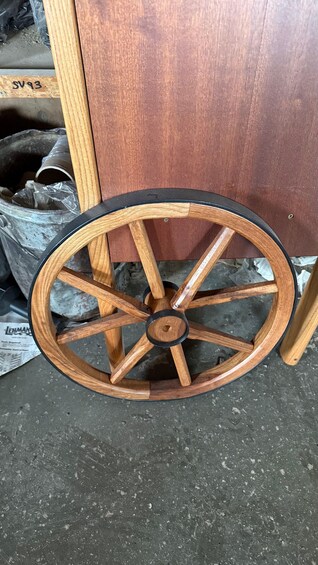 A wooden wheel with a black rim, possibly part of a cart or carriage, on a concrete surface. 5