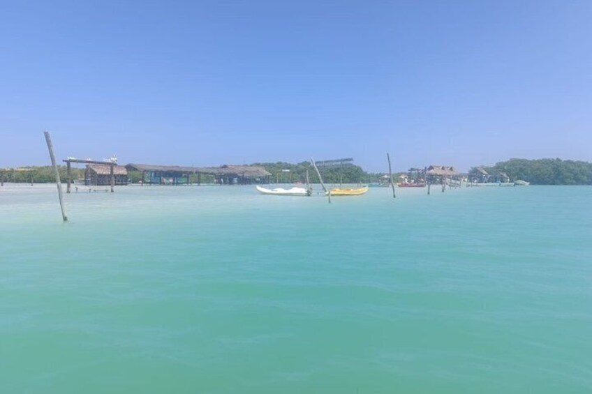 A calm sea with a small boat, a pier, and buildings in the background. 4