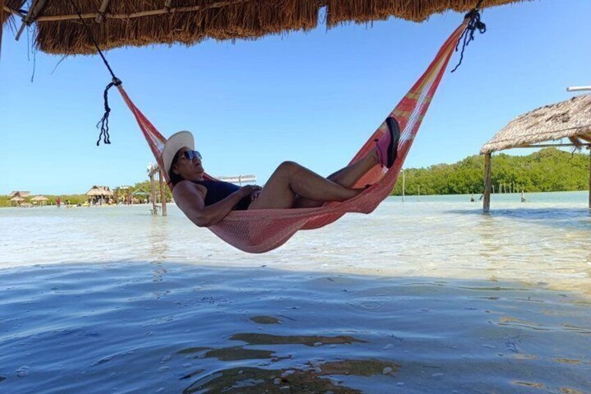 A person relaxing in a hammock on a beach with clear water and a thatched roof structure in the background. 2