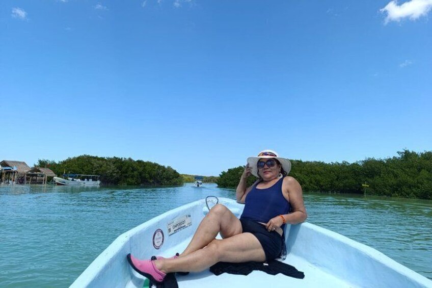 A person in a boat on a calm body of water, surrounded by greenery and a clear sky. 3