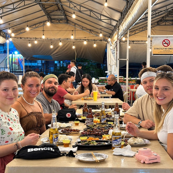 A group of people dining at an outdoor event with tables set with food and drinks. 3