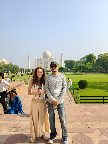 A couple standing in front of the Taj Mahal with a well-maintained garden and clear sky in the background. 2
